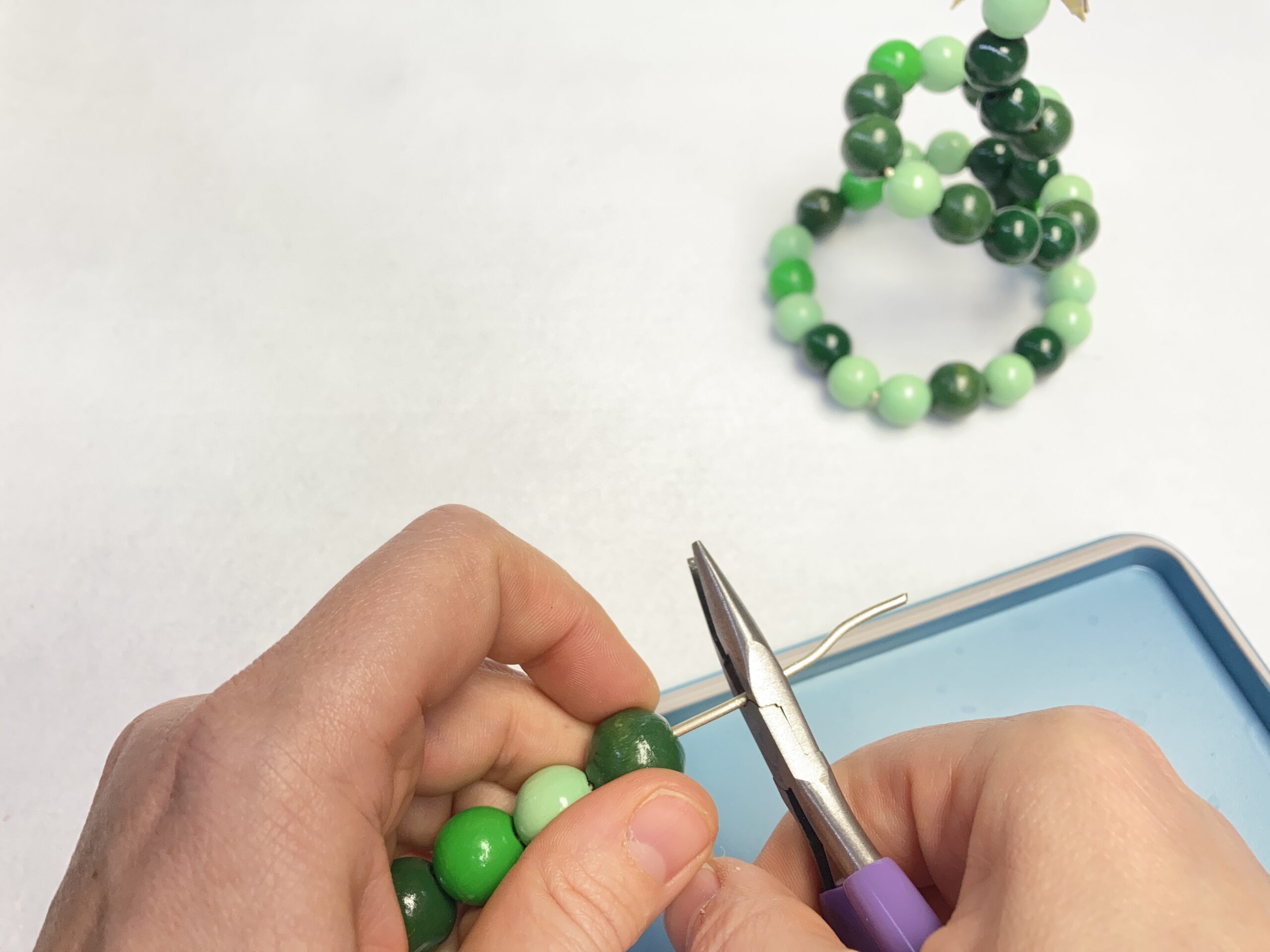 Draht mit Holzperlen wird auf die richtige Länge mit einer Zange gekürzt