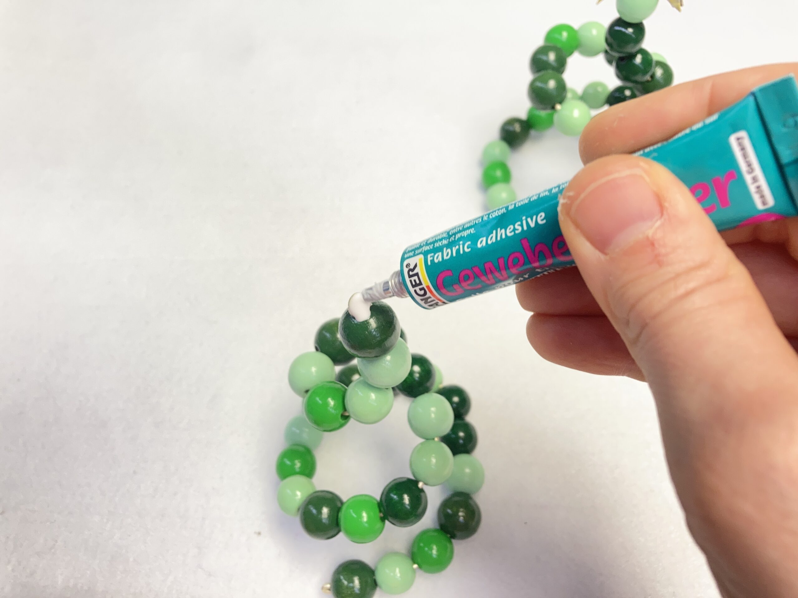 Auf die Spitze einer Holzperlenspirale wird Kleber aufgebracht