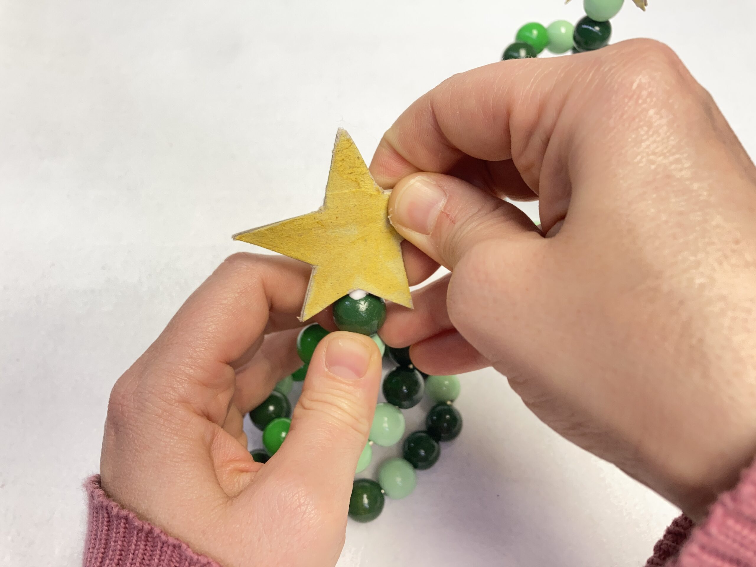 An die Spitze eines Spiralenförmigen Holzperlenbäumchens wird ein Stern angeklebt